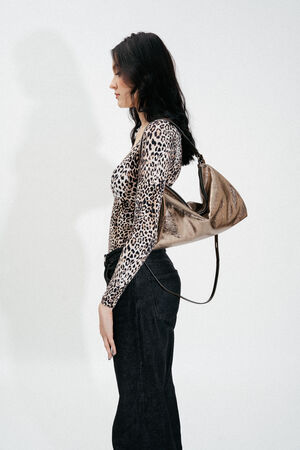 Weiblich gelesenes Model mit dunklen Haaren trägt goldene Ledertasche auf der Schulter