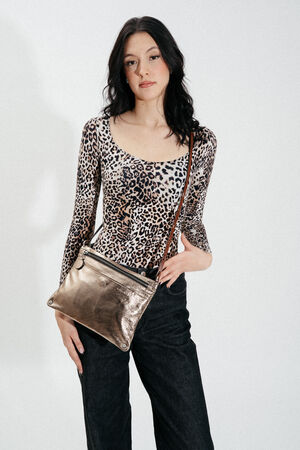 Woman wearing a leopard print top and black pants stands holding an INA KENT metallic crossbody bag against a plain white background.