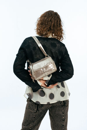 Weiblich gelesenes Modell mit goldener Tasche auf der Schulter