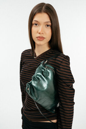 Weiblich gelesenes Model mit grüner Ledertasche auf der Schulter