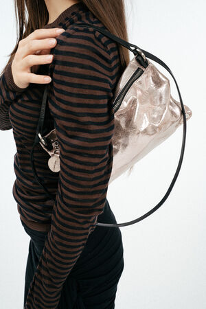 Weiblich gelesenes Model mit rosa, glänzenden Ledertasche auf der Schulter