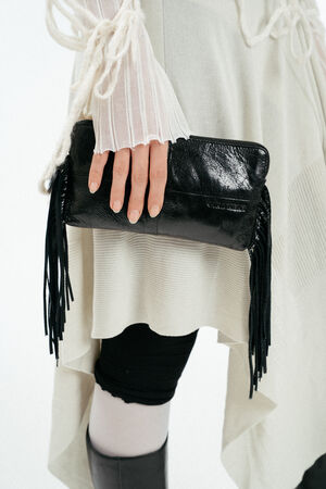 Weiblich gelesenes Modell hält in der Hand schwarze, kleine Ledertasche mit Fransen