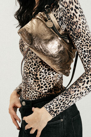 Woman wearing a leopard print long-sleeve top, black jeans, and an INA KENT metallic gold crossbody bag across her chest.