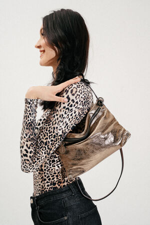 Woman in a leopard print top and black jeans standing sideways with an INA KENT metallic shoulder bag resting on her shoulder.