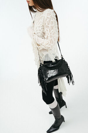 Weiblich gelesenes Model in losem, weißen Strick, mit schwarzer Ledertasche mit Fransen Crossbody getragen