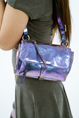 A person wearing a gray dress holds an INA KENT shiny, iridescent purple shoulder bag with a buckle and strap detail.