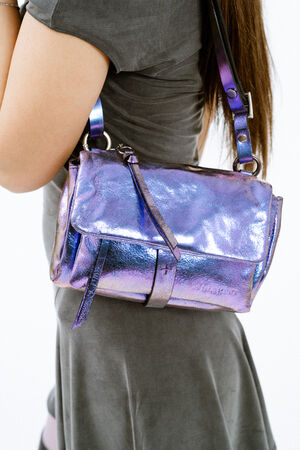 A person wearing a gray dress carries an INA KENT shiny, metallic purple shoulder bag with a strap and buckle detail.
