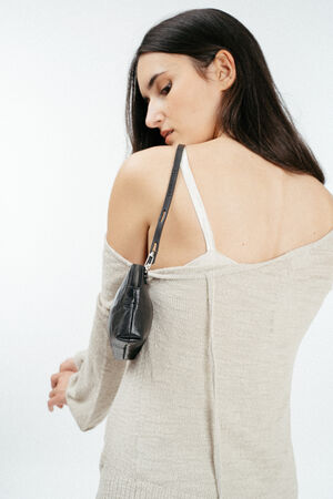A woman with long dark hair wears an off-the-shoulder beige sweater, exposing a white bra strap, and carries a chic black INA KENT handbag over her shoulder.
