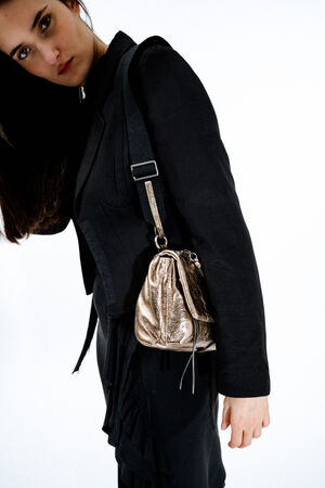 Woman in a black blazer carries an INA KENT metallic gold drawstring handbag on her shoulder, standing against a plain white background.