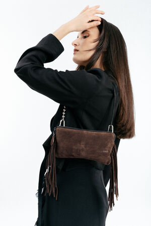 A woman wearing a black outfit poses in profile with one hand on her forehead, carrying an INA KENT brown suede handbag with fringe details over her shoulder.