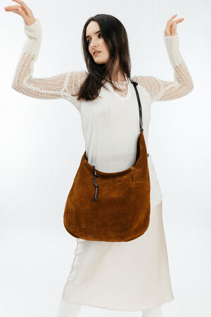 Woman wearing a white outfit poses with a large brown INA KENT suede shoulder bag, featuring a black strap and metal hardware, against a plain light background.