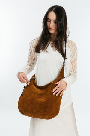 A woman with long dark hair wearing a white outfit holds a large brown INA KENT suede shoulder bag against a plain light background.