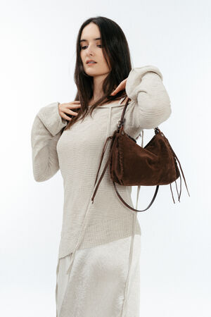 A woman wearing a light-colored, long-sleeve knit top and skirt holds an INA KENT brown suede handbag over her shoulder against a plain white background.