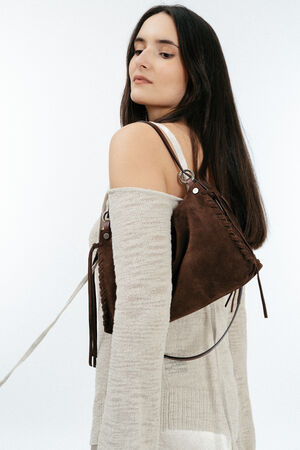 Woman wearing a beige off-shoulder sweater and white top, carrying an INA KENT brown suede purse over her shoulder, looking slightly away from the camera.