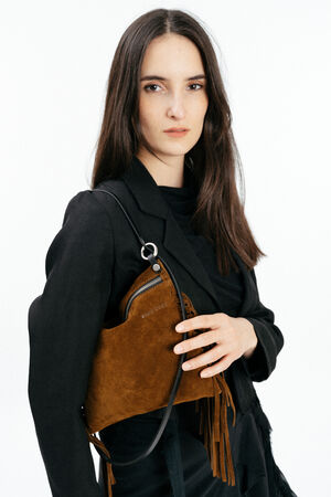 Woman with long brown hair wears a black blazer and holds an INA KENT brown suede bag with fringe and a black strap against a plain white background.