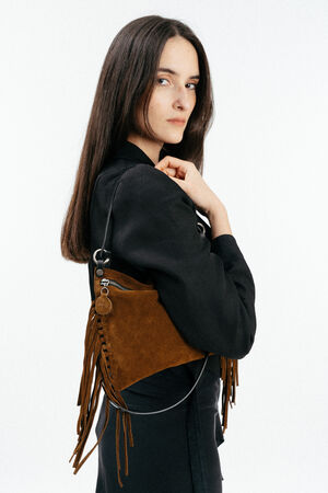 A woman in a black outfit poses with an INA KENT brown suede fringe handbag over her shoulder against a plain white background.
