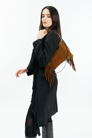 Woman in a black outfit holds an INA KENT brown suede fringe bag over her shoulder, standing against a plain white background.