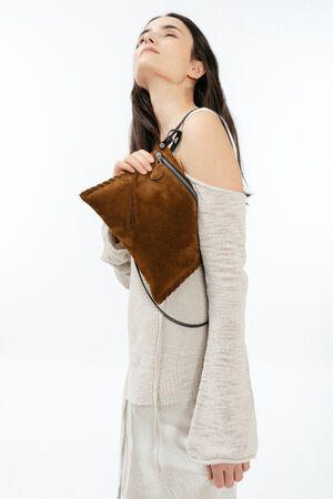 A woman in a cream-colored off-shoulder sweater holds an INA KENT brown suede handbag against her chest, looking upward with eyes closed against a plain white background.