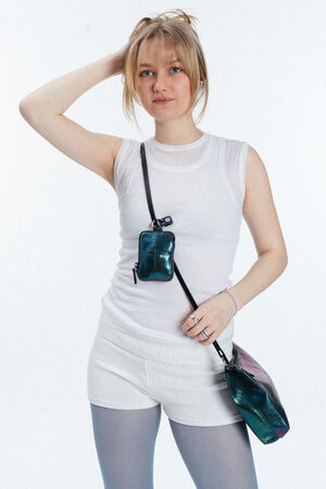 Eine Frau, die ein ärmelloses weißes Oberteil und weiße Shorts trägt, posiert mit einer Hand in ihrem Haar und trägt zwei schillernde blaue INA KENT-Taschen mit schwarzen Trägern quer über den Körper.