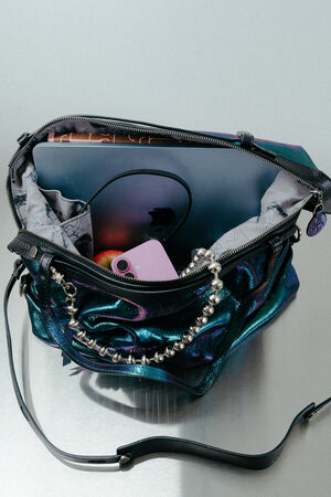 An open iridescent INA KENT handbag containing a silver laptop, a pink smartphone, and a beaded strap sits on a light-colored surface.