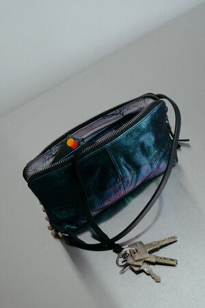 Eine schillernde INA KENT Geldbörse mit Reißverschluss und Handgelenkschlaufe ruht auf einer reflektierenden Oberfläche, an der ein Schlüsselbund befestigt ist.