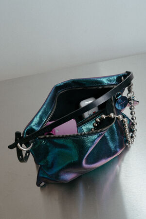 Ein metallisch blaues INA KENT Portemonnaie liegt offen auf einer spiegelnden Oberfläche und gibt den Blick auf seinen Inhalt frei, darunter ein Telefon, eine Kette, ein Schlüsselbund und eine lavendelfarbene Karte.