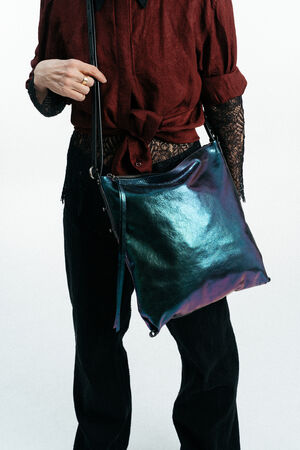 Person, die eine burgunderrote Bluse mit schwarzen Spitzenärmeln trägt, hält eine glänzende, schillernde INA KENT Crossbody Bag. Das Foto ist an den Schultern und Knöcheln abgeschnitten.