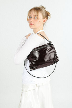 A woman in a white outfit looks over her shoulder, modeling an INA KENT shiny dark brown shoulder bag with a circular handle.