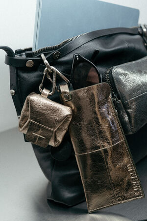 An INA KENT black leather bag with a laptop inside, a metallic gold pouch, sunglasses in a gold case, and a small gold accessory attached to the handle.