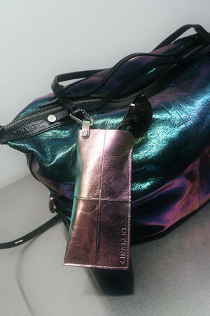 A metallic iridescent INA KENT bag sits on a surface with a shiny pink eyeglass case and a pair of sunglasses resting on top.