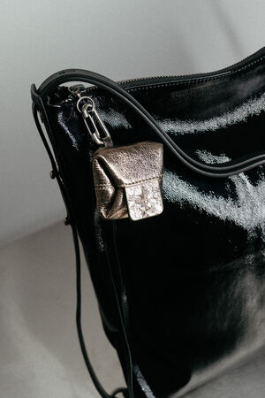 A close-up of a shiny black INA KENT handbag with a metallic silver mini pouch attached to its zipper.