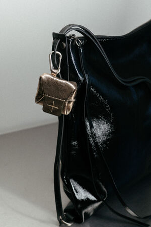 A small metallic pouch by INA KENT hangs from the handle of a large black leather bag, attached by a metal clasp against a neutral background.