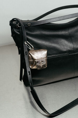 Black leather shoulder bag by INA KENT with a long strap, featuring a small metallic pouch attached to the strap.