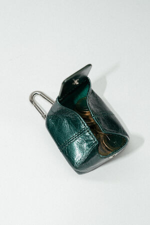 A small, open green leather INA KENT coin pouch with a metal clip, containing several coins, placed on a plain white surface.