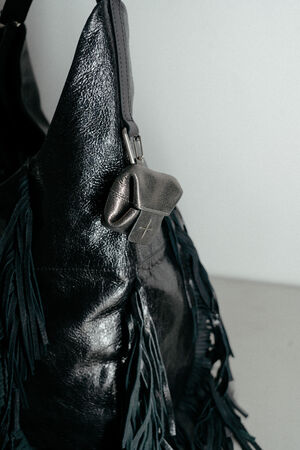 Close-up of an INA KENT black leather bag with fringe detailing and a small pouch attached near the top handle.