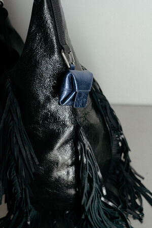 A textured black fringed INA KENT bag with a small blue leather pouch attached to the strap, set against a plain light background.