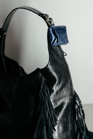 A close-up of a black leather INA KENT bag with fringe detailing, featuring a small blue leather pouch attached to the handle.
