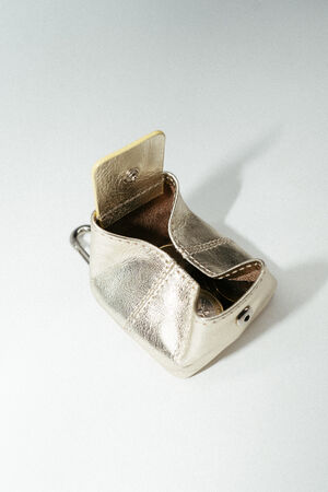 A small metallic gold INA KENT coin purse with an open flap, revealing a yellow card partially inside, placed on a light surface.
