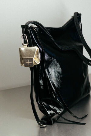 A shiny black leather INA KENT handbag with thin straps sits on a surface. A small metallic gold purse with a clasp is attached to one of the bag’s handles.