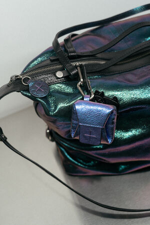 Iridescent INA KENT bag with black straps and a small metallic blue mini-backpack keychain attached to the zipper.