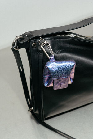 A small iridescent purple pouch with a clasp is attached to the zipper of an INA KENT black leather handbag.