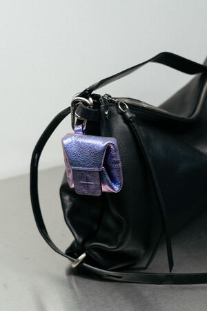 A small, metallic purple INA KENT pouch is attached to the zipper of a black leather bag with a metal clasp.