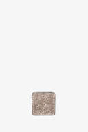 A small, rectangular, textured metallic tag from INA KENT with a hole at the top center, positioned against a plain white background.