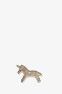 A small, metallic unicorn-shaped object with a hole in its center is displayed on a plain white background, reflecting the playful yet elegant design signature of INA KENT.