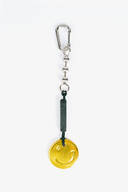 A keychain by INA KENT with a silver carabiner, a black tag, and a gold smiley face charm on a black cord, displayed on a white background.