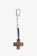 A metal keychain with a silver carabiner clip and a brown leather cross-shaped pendant attached by a black strap, crafted in the signature minimalist style of INA KENT.